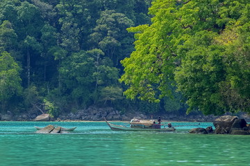 view of Moken's boat floating seaside in blue-green sea with green forest background, Khao Chong Kad Bay, Surin island, Mu Ko Surin National Park, Phang Nga, southern of Thailand.