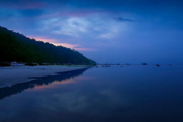 Sea view morning of white sand beach with mountain around with soft mist and red sun light in cloudy sky background, twilight at Khao Chong Kad, Surin island, Mu Ko Surin National Park, Thailand.