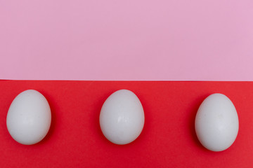 Three Easter holiday flat lay with white egg on a solid bright red and pink pastel and vibrant background with copy space.