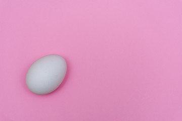 Easter holiday flat lay with white egg on a solid pink pastel background with copy space.