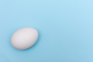 Easter holiday flat lay with white egg on a solid light blue pastel background with copy space.