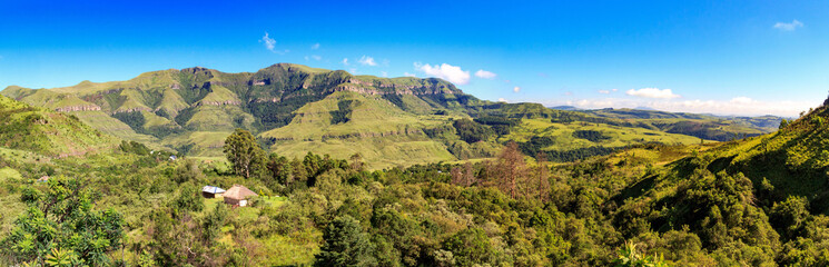 Fototapeta na wymiar Panoramic view over a forest with a little hut embedded and green mountains, sunny day, Drakensberg, Giants Castle Game Reserve, South Africa