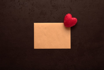 Red heart on blank kraft card for Valentine's day message on black background. Declaration of love concept. Top view. Flat lay