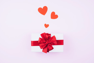 Gift box with a red bow and hearts on a soft pink background.