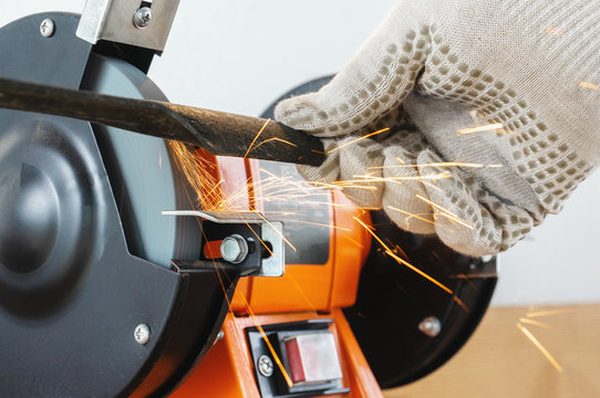 Sharpening The Blade Of A Lawn Mower With An Electric Sharpener. Hands In Work Gloves Hold And Sharpen The Blade