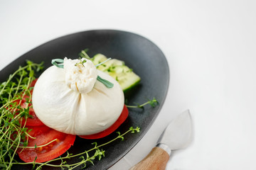 fresh Italian burrata cheese with tomato slices on a black plate on a white background. Selective focus. Copy space