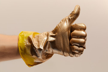 Image of gold painted Like gesture of hand in yellow rubber glove on light beige background