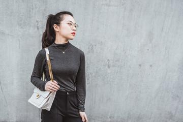 Urban young woman leaning on gray wall with shoulder bag