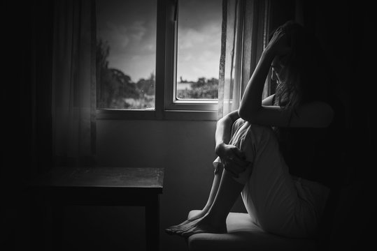 depress woman sitting on chair in room near window in white tone, sadness and depress concept