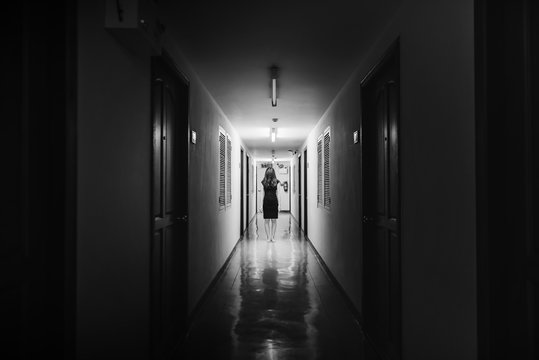 Horror photo of woman with long hair walking on corridor in white tone
