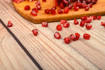 Pieces of ripe juicy pomegranate and pomegranate seeds on a wooden Board on a wooden background. Close up.