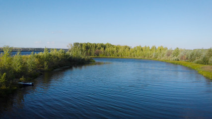 aerial view of calm small river and trees on shores in sunny weather in summer, camera is flying along coasts