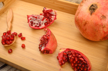 Ripe juicy pomegranate, pomegranate slices and pomegranate seeds in a wooden spoon on a wooden tray on a wooden background. Close up.