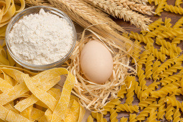 Organic food. Variety of types and shapes of dry Italian pasta.  Eggs and flour,  sprigs of wheat. Close up.