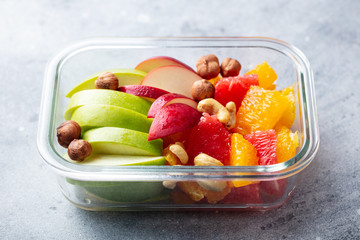 Fruits salad and nuts in a glass container. Healthy eating. Grey background. Close up.
