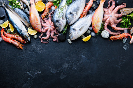 Fresh fish and seafood assortment on black slate background. Top view. Copy space.
