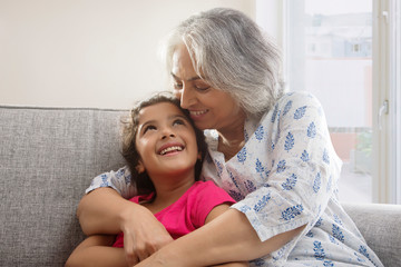 Portrait of a grand-daughter and grandmother sitting on the couch at home. 	