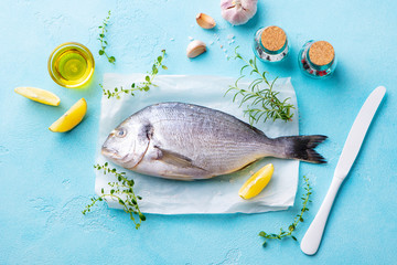 Dorado fish with cooking ingradients on a parchment paper. Blue stone background. Top view.
