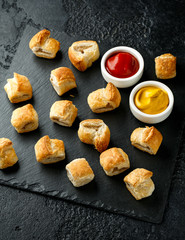 Pork sausage rolls with mustard and ketchup on rustic black stone