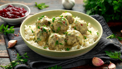 Hot Swedish meatballs with white rice and cranberry sauce on wooden table