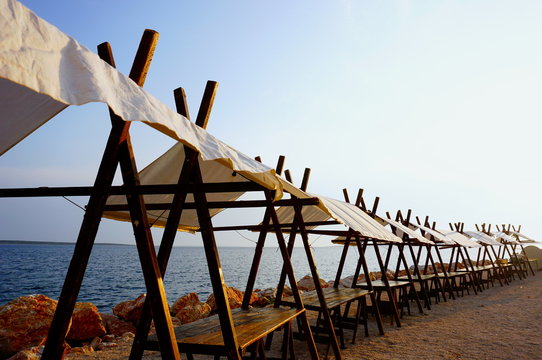 Market stalls on the pebble beach in front of the blue sea surface. Empty stalls were prepared for summer festival in the village by the sea