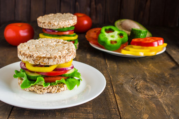 healthy vegetarian burger with rice cakes lettuce bell pepper cucumber tomato red onion on plate and sliced ingredients close up