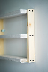 Empty white wooden pine shelves on white wall background.