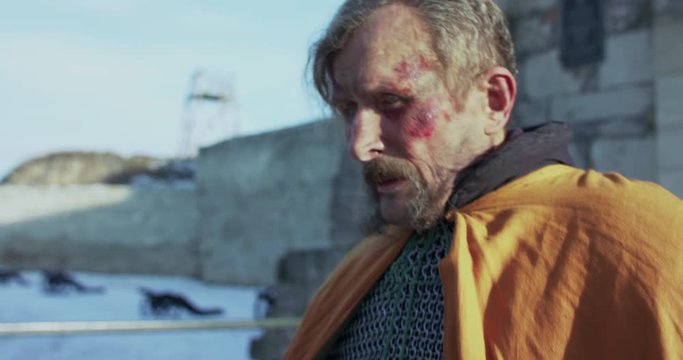 Old, wounded hetman in armor with sword walks at fortress and looks around