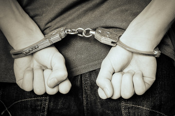 Monochrome image. The criminal was detained by the police. The handcuffed hands clenched into fists.