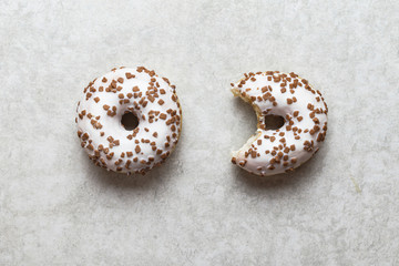 Whole and bitten donuts on a light grey background. Creative commision concept.