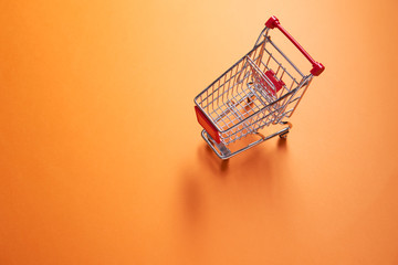 Iron small supermarket trolley on empty orange background