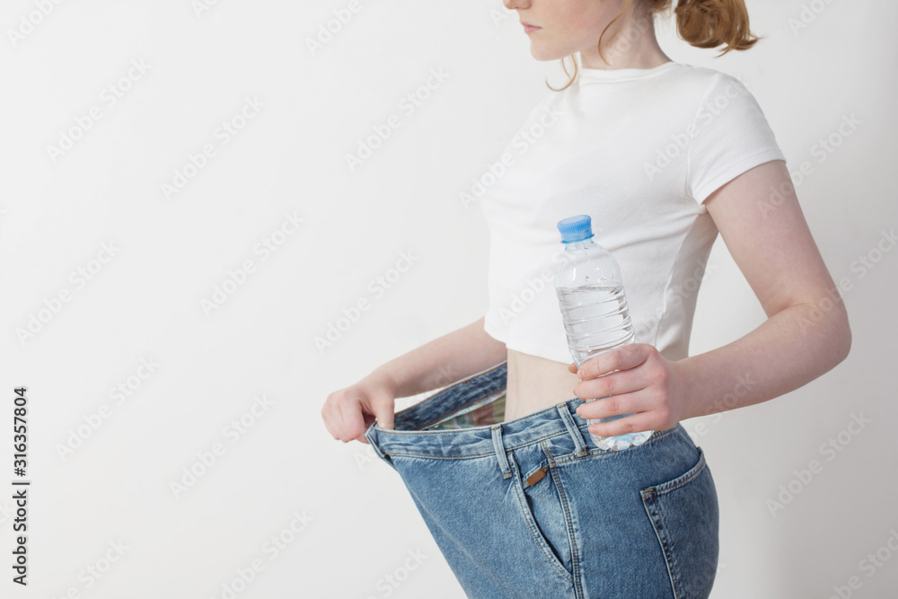 Wall mural girl with water in bottle pulling her big jeans and showing weight loss