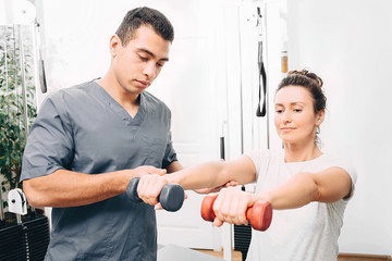 Physiotherapist helps a woman do physical exercises to treat inflammation of the joints in her arms...