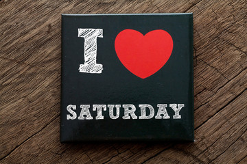 I Love Saturday written on black note with wood background