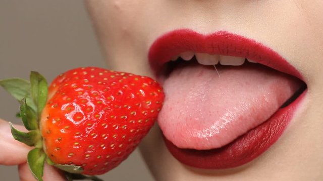 Woman imitates masturbation. Sensual red lips is licking strawberry. Sexy woman's tongue and lips