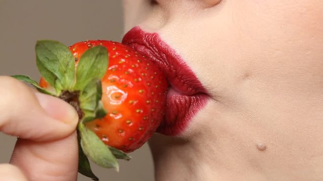 Woman imitates masturbation. Sensual red lips is licking strawberry. Sexy woman's tongue and lips