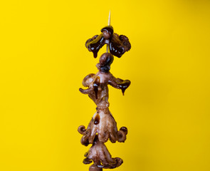 kushiyaki fried octopus doused with sauce on a skewer, five pieces on a yellow background, marine delicacy