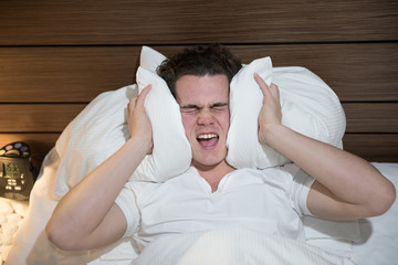 young caucasian man in bad sleeping holding pillow silence noise trying to sleep