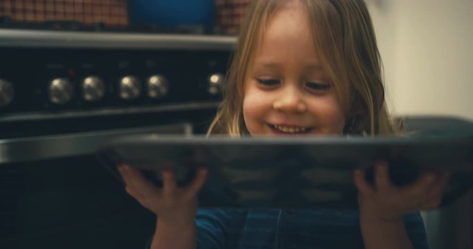 Little toddler helping his mother put a tray of cookies in the oven