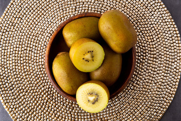 Golden kiwis in the wooden bowl on the golden background