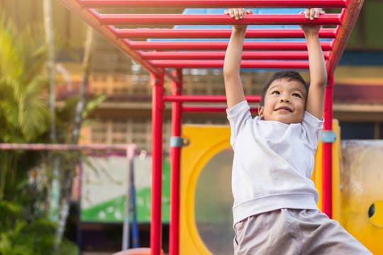 Soft​ focus.​ Kid exercise for health and sport concept. Happy Asian student​ child boy playing and hanging from a steel bar at the playground. 5 years old.