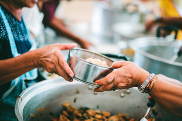 The hands of the poor handed a plate to receive food from volunteers to alleviate hunger, the concept of helping the homeless.