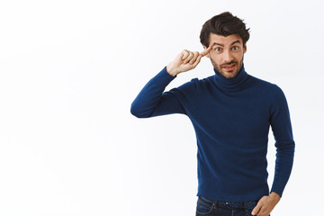 Annoyed, bothered good-looking bearded man in high neck sweater, roll finger over temple and stare...