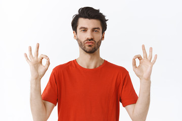 Naklejka premium Confident, sassy young good-looking man with brisle, look like macho, have everything under control, show okay ok, good gesture, squinting look serious and determined camera, white background