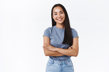 Cheerful asian brunette woman in t-shirt, cross hands over chest in casual pose, tilt head and...