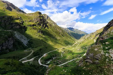 Fotobehang Panoramic view of a valley in the Pennine Alps with a winding road, green alpine pastures under a blue sky with some white clouds on a summer day. Lac de Moiry, Grimentz, Valais, Switzerland © Steven