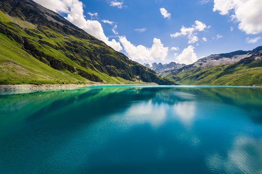 Mountains reflect in the clear blue water of the mountain lake Lac de Moiry in the Pennine Alps on a summer day with a nice blue sky and some white clouds. Grimentz, Valais, Switzerland