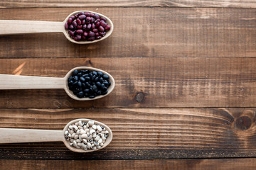 Three large wooden spoon with beans on wooden background