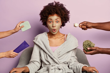 Young surprised woman takes care of her skin, cleans pores with facial mud mask, wears domestic...