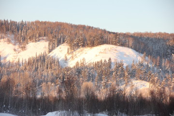 snow-covered hills, evergreen trees on the slopes, in the sunset. Lots of snow and frost trees.